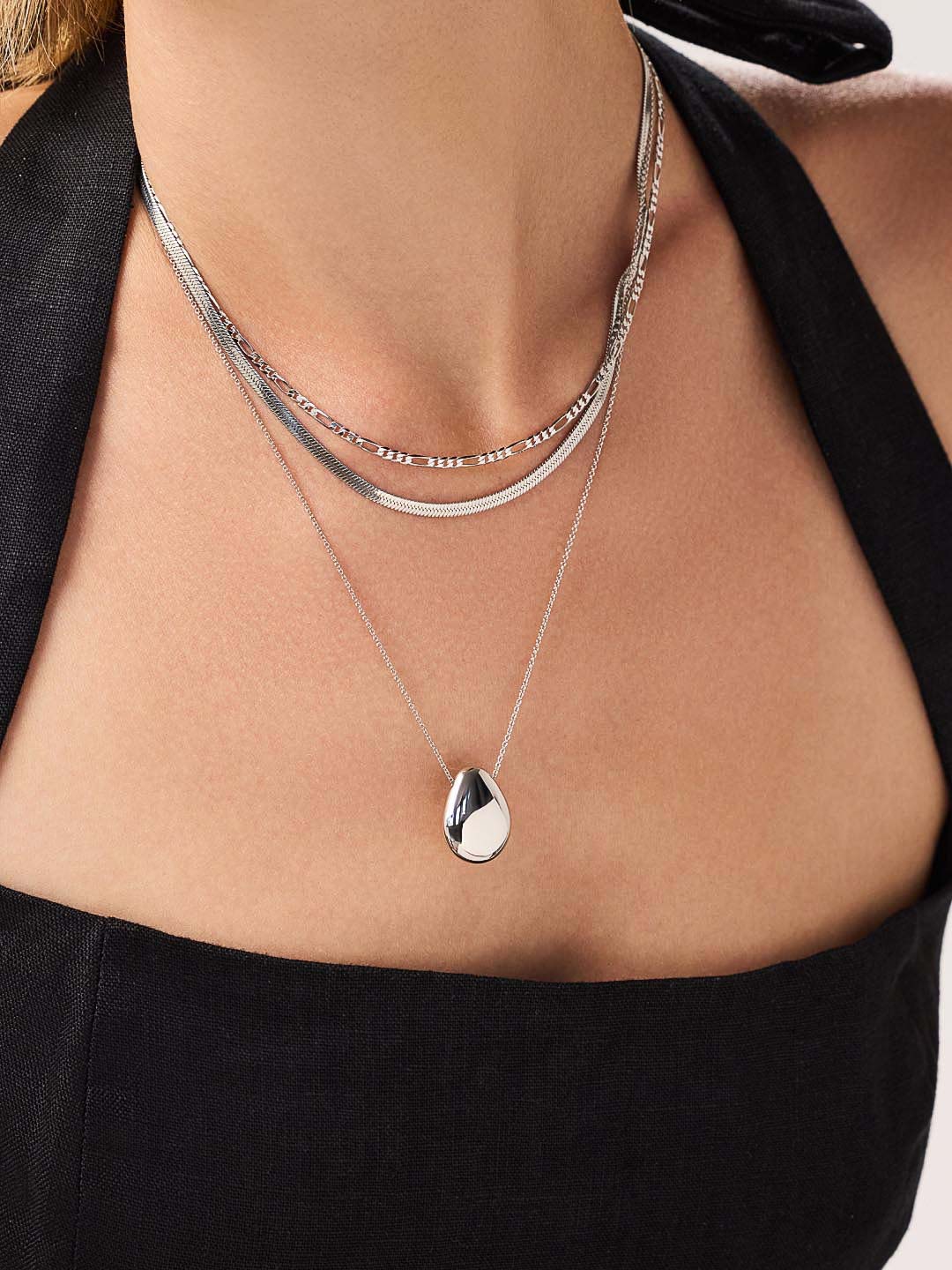 Silver pendant necklace worn with two other chain necklaces