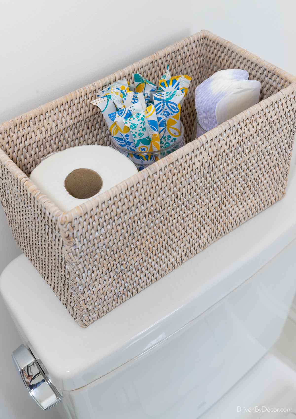 Woven storage box on toilet tank holding toilet paper and menstrual products