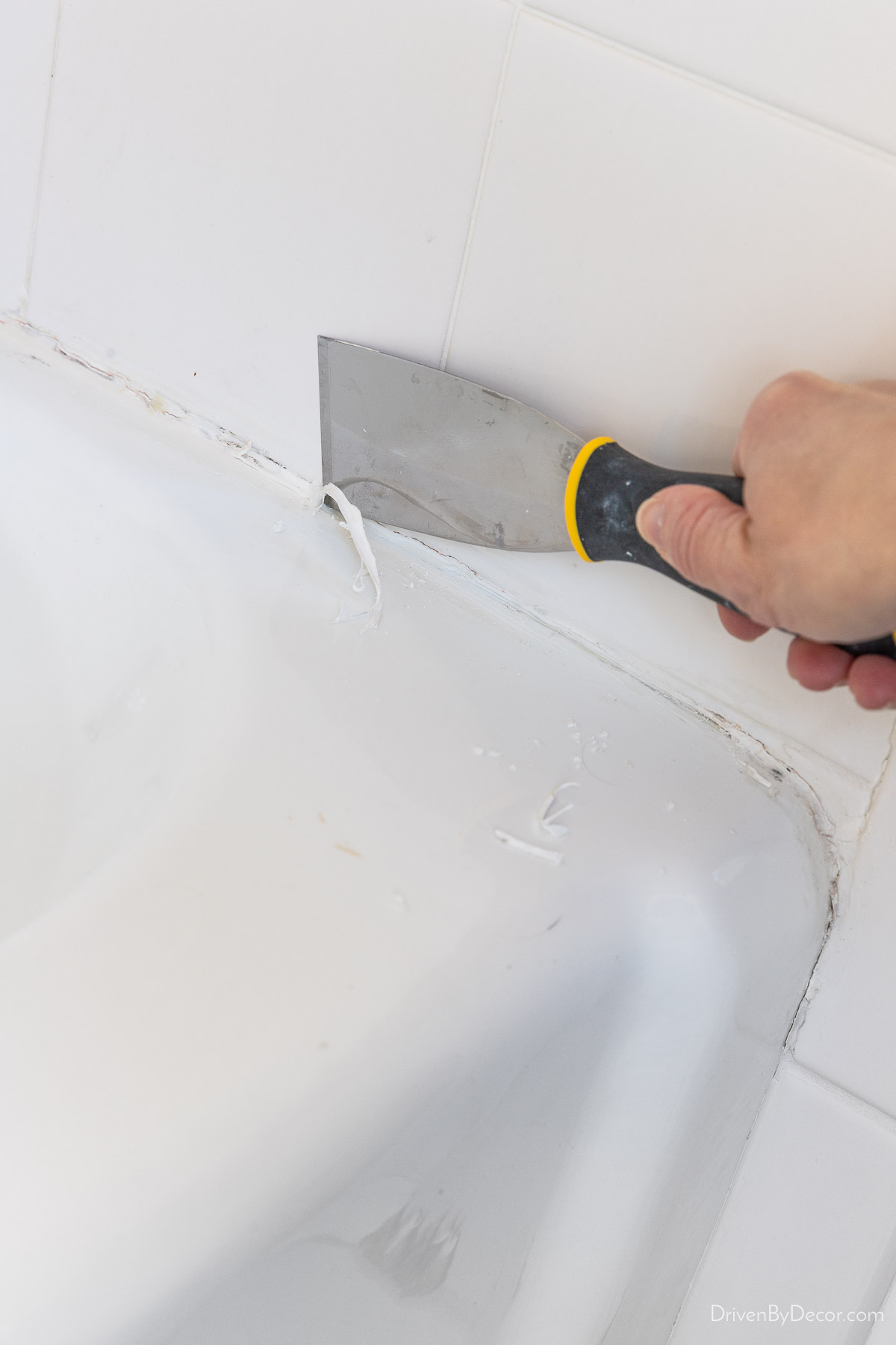 Using putty knife to scrape old caulk off of bathtub