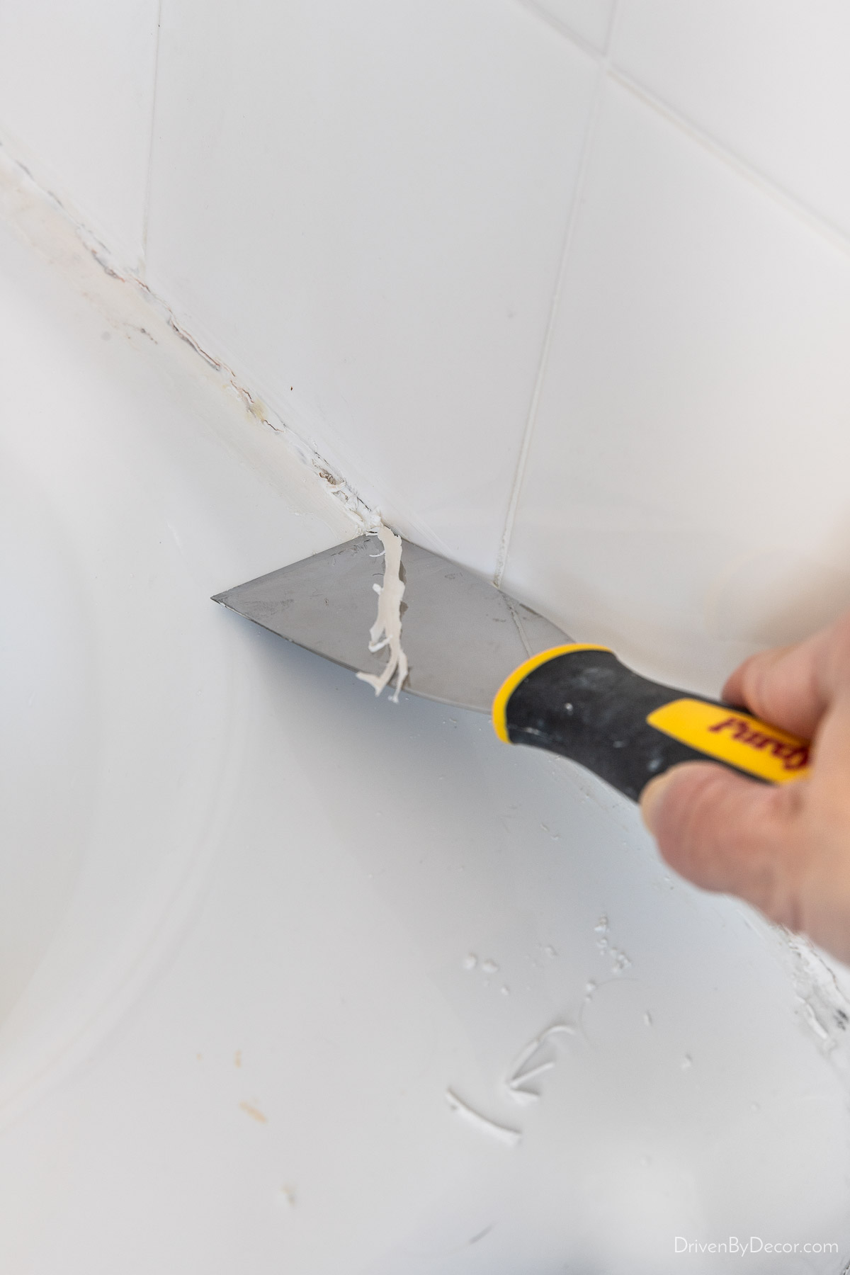 Using a stiff putty knife to scrape off old caulk on bathtub