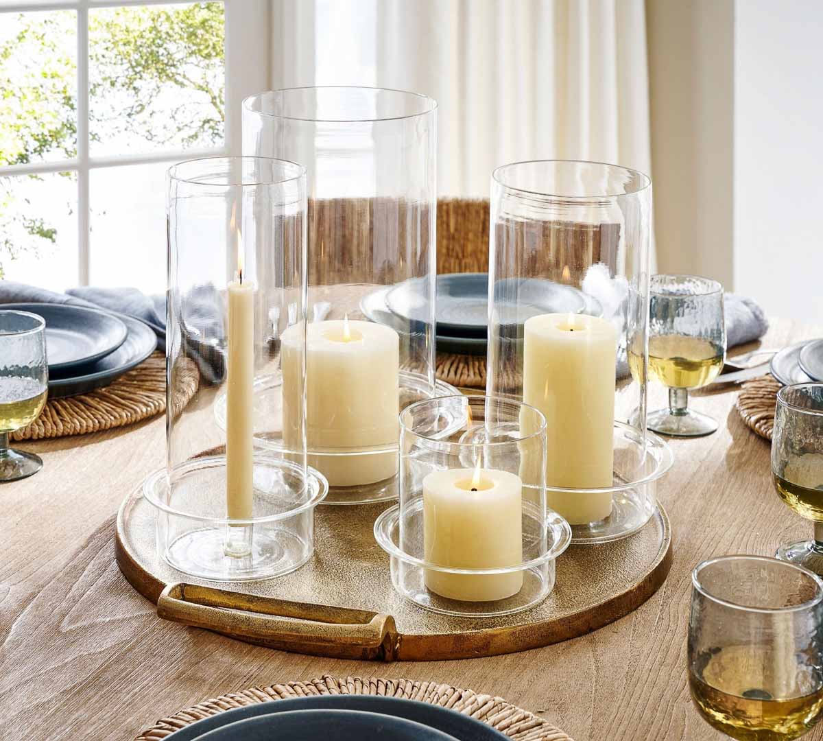 A grouping of glass hurricanes on a tray in the center of a dining table