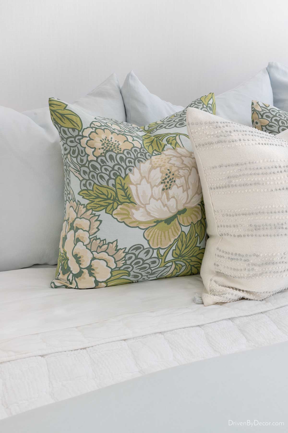 Light blue Euro shams, patterned pillows, and white textured pillows on bed