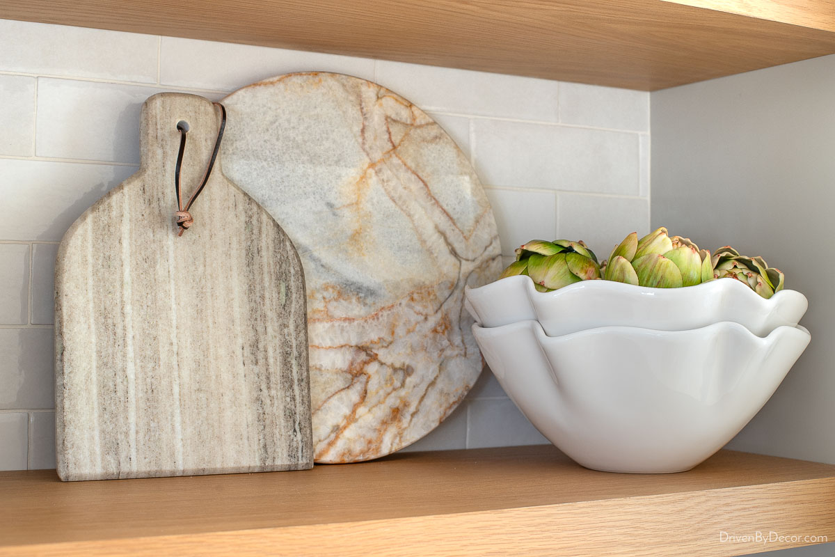 Marble cutting boards and scalloped bowls on kitchen coffee bar shelves