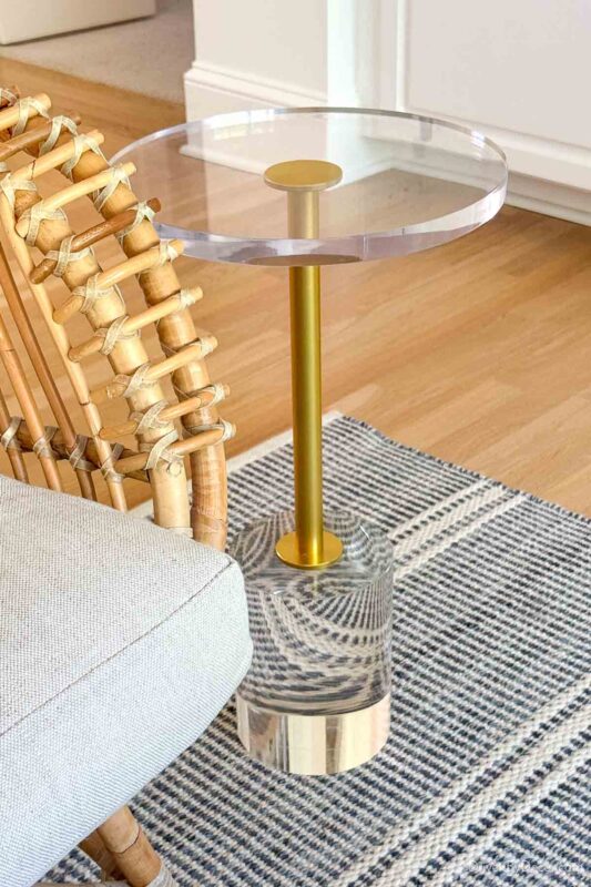 Round acrylic side table next to rattan chair