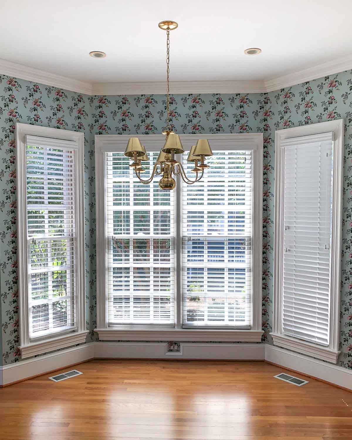 Our breakfast nook when we moved in with green floral wallpaper and brass light fixture
