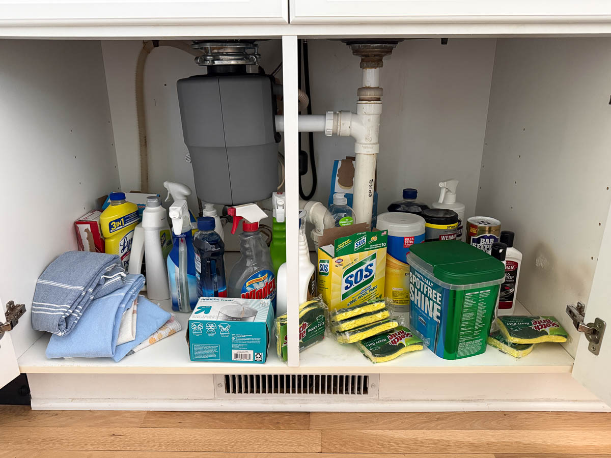 Mess under kitchen sink with cleaners, sponges, and more