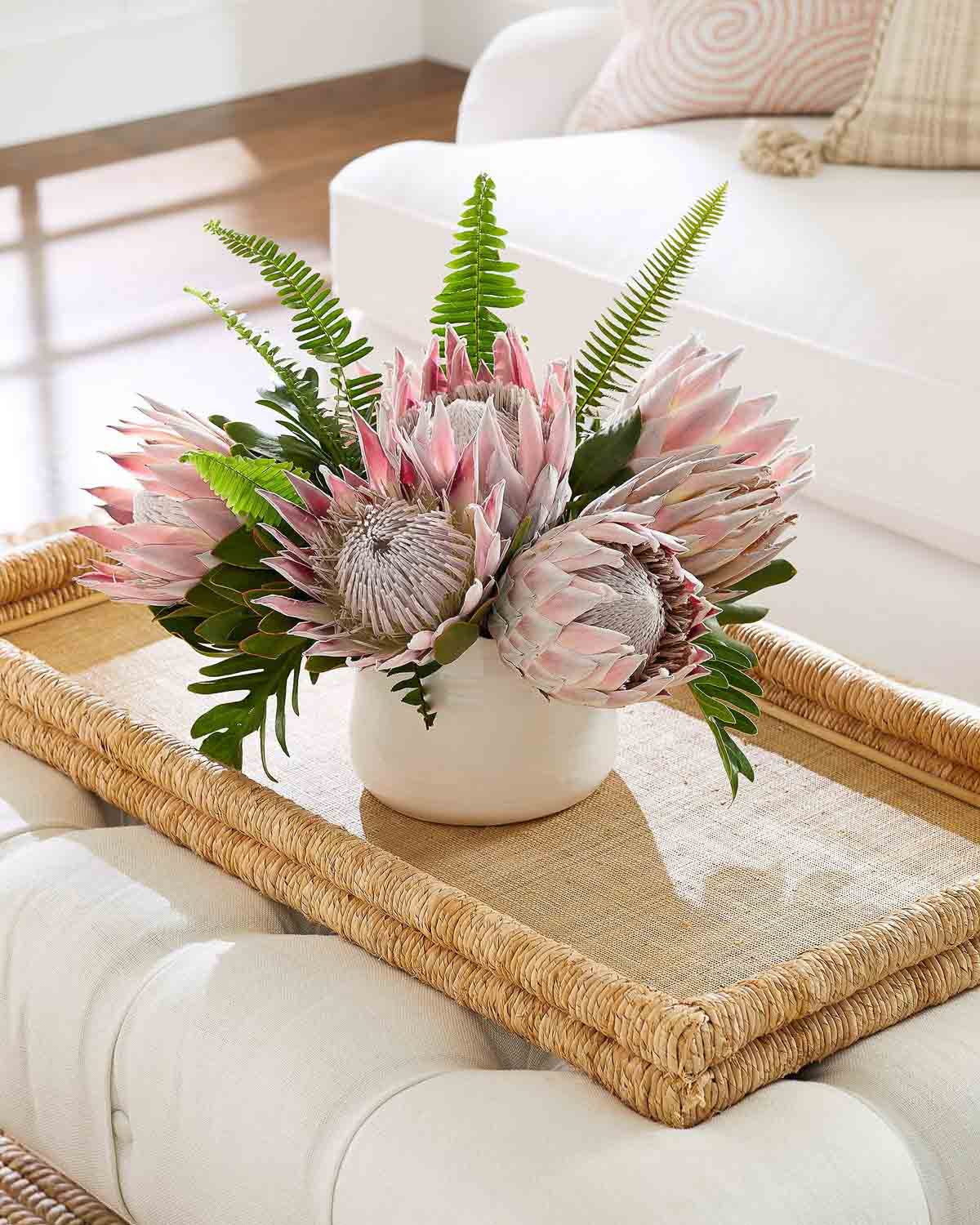 Large woven tray sitting on ottoman with a vase of flowers